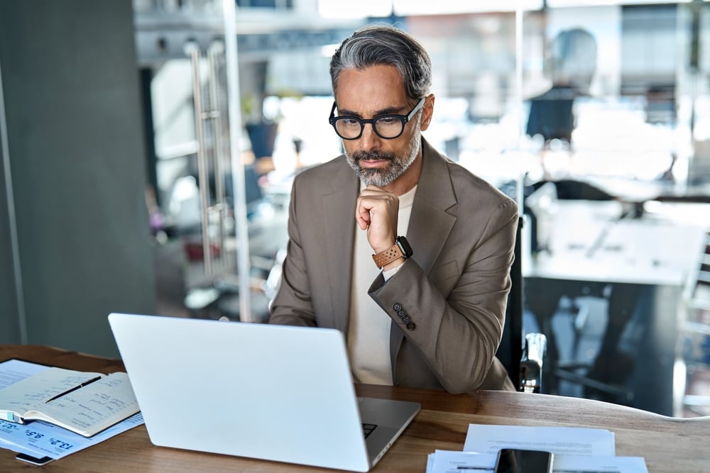 Middle-aged business professional working on laptop, thinking.