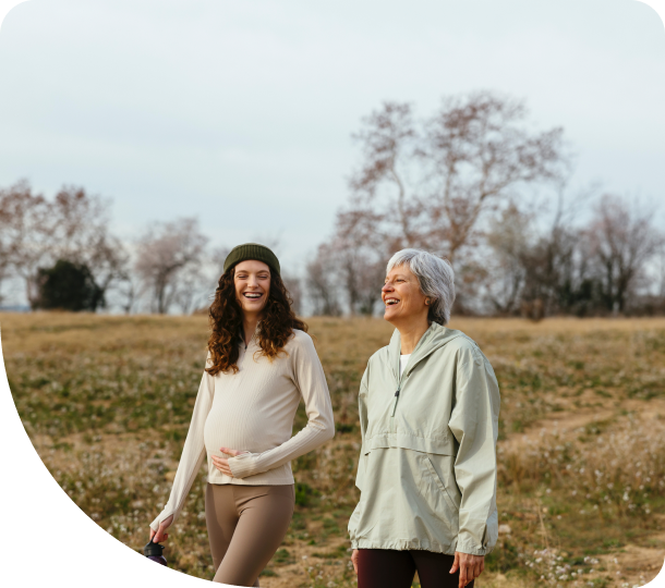 Two women stroll through a lush green field, enjoying a sunny day and the beauty of nature around them.