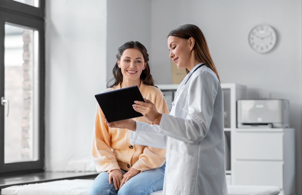 Female doctor with tablet pc computer talking to smiling woman patient at hospital