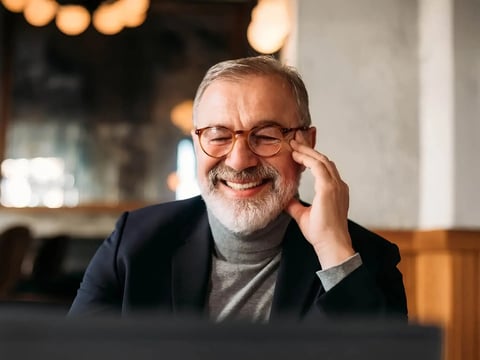 Older man with beard wearing glasses smiling at computer screen