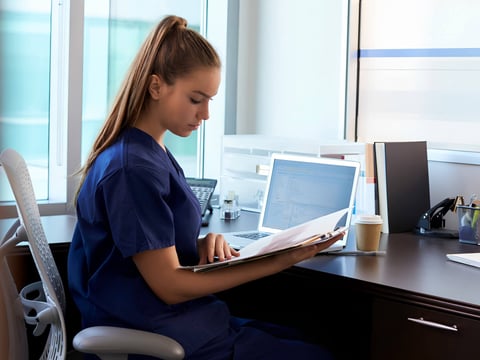 Young medical professional in scrubs sitting at a desk looking at paperwork