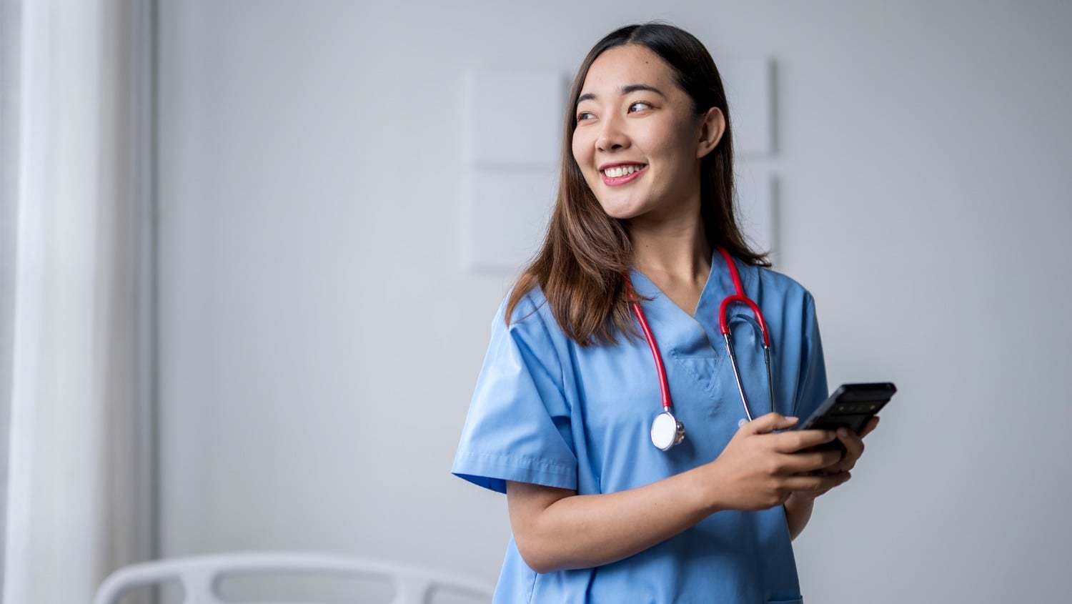 Happy young nurse using smartphone in hospital room-1-1