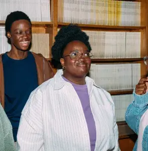Three women stand together in front of a large bookshelf filled with various books, engaged in conversation.